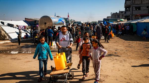 Youssef Al-Khishawi, an MSF water and sanitation agent, helps children carry water to their tent in the Tal Al-Sultan area of the southern Gaza town of Rafah, on January 27, 2024.